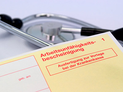 Ein gelbes Formular mit der Aufschrift "Arbeitsunfähigkeitsbescheinigung" und einem Stethoskop im Hintergrund.